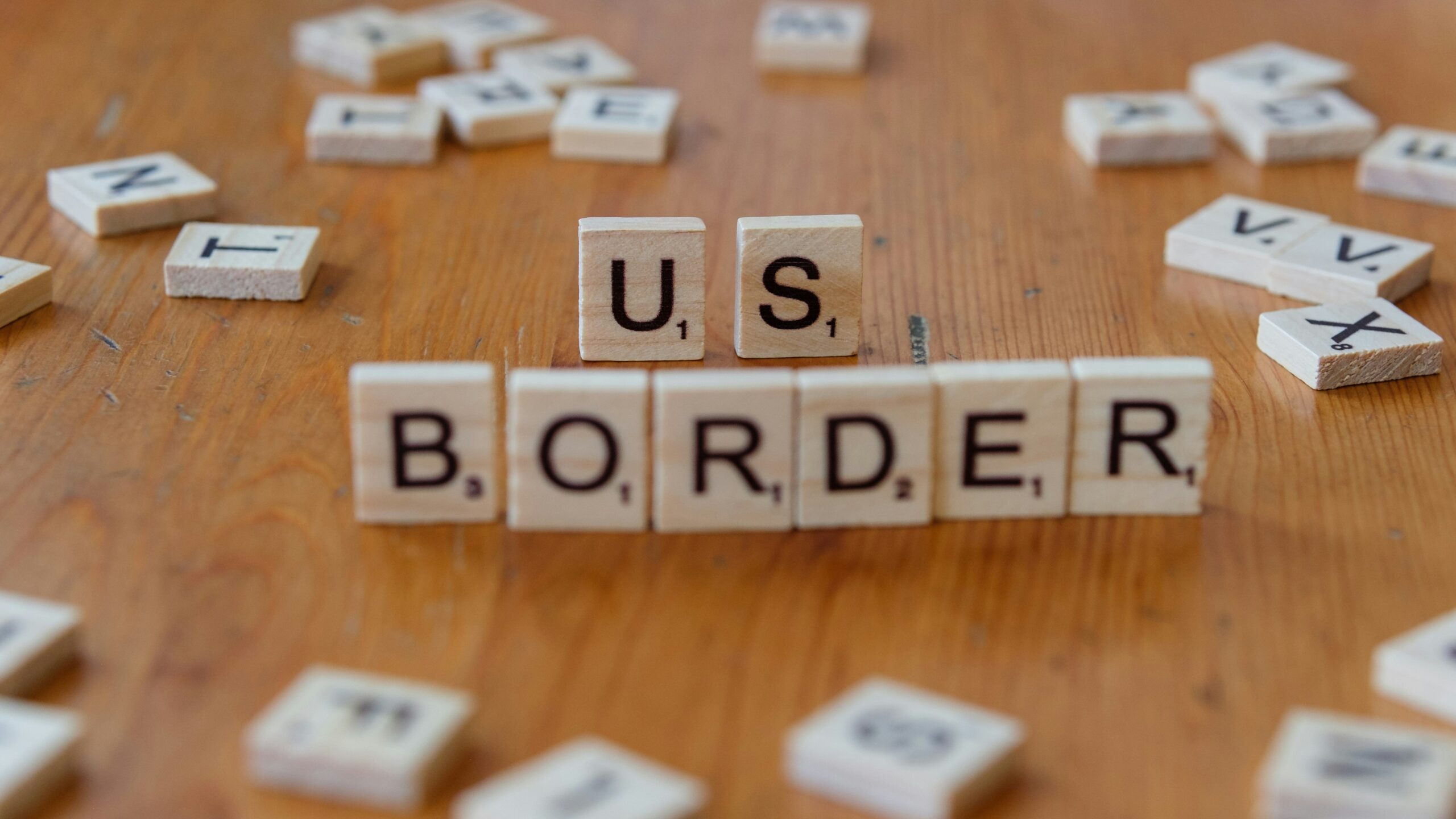 A wooden table topped with scrabble tiles spelling us border